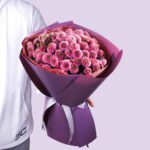 A large bouquet of pink chrysanthemums wrapped in purple paper with a white ribbon.