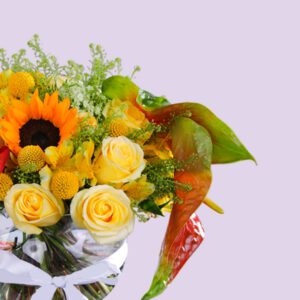 A vibrant bouquet of sunflowers, roses, and other colorful flowers arranged in a glass vase with a white ribbon.
