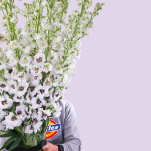 A man holding a giant bouquet of white delphinium flowers, which cover his face.