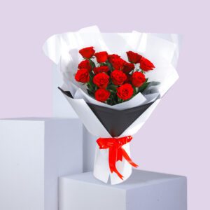 A bouquet of red roses wrapped in white paper with a black accent and a red ribbon.
