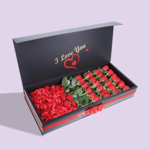 A black gift box open to reveal a compartment of red roses and another compartment of red rose petals. The lid of the box has the words "I Love You" printed on it.