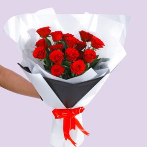 A bouquet of red roses wrapped in white paper with a black accent and a red ribbon.