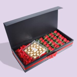 A black gift box open to reveal a compartment of red roses and another compartment of Ferrero Rocher chocolates.