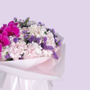 A bouquet of pink orchids and white hydrangeas wrapped in white paper with a pink ribbon.