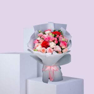 A bouquet of mixed roses in shades of pink and red, wrapped in white paper and tied with a pink ribbon.