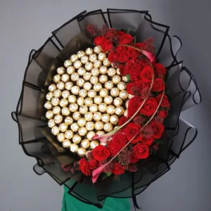 The image shows a large and luxurious bouquet filled with Ferrero Rocher chocolates and red roses. The bouquet is wrapped in black netting and tied with a ribbon.