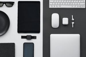 The image shows a flat lay of various tech gadgets and accessories on a black and white background.