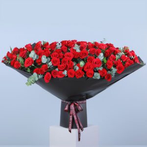 A massive bouquet of vibrant red roses with some eucalyptus leaves, wrapped in black paper and tied with a dark ribbon