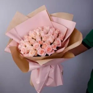 A large bouquet of light pink roses wrapped in brown and pink paper, held by an arm.