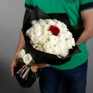 A bouquet of white roses with a single red rose in the center, wrapped in black paper