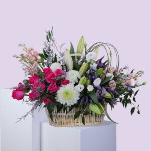 A woven basket filled with an arrangement of pink and white flowers, including Garden roses, Eustoma, and possibly Tulip
