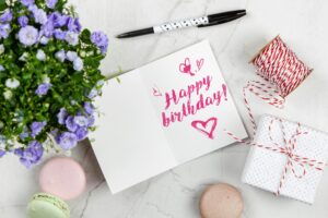 In the center, an open greeting card displays the handwritten message "Happy birthday!" in bright pink ink, adorned with small heart doodles
