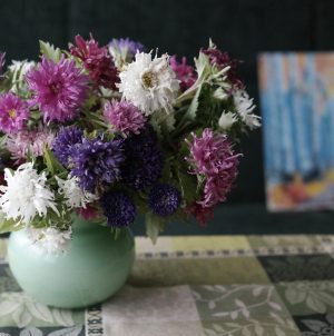 a bouquet of colorful aster flowers in a light green, round vase